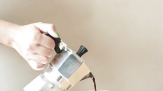 A person pouring black coffee into clear glass