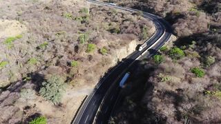 Transport trucks gliding over black asphalt road among arid vegetation