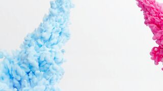 Blue and pink paint enter the transparent liquid creating flowing clouds over a white background