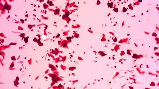 Metallic heart shaped confetti falling in slow motion over a pink background